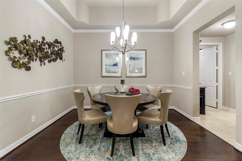 This dining room features wood floors, tray ceilings, crown molding, chair rail, and a chandelier.