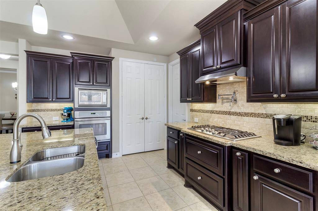 The kitchen features stainless steel appliances, tile floors, tile backsplash, and a pot filler above the gas cooktop.