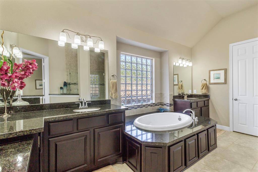 Indulge in luxury in this meticulouslydesigned primary bathroom featuring tile floors, wood cabinets, dual sinks, and a soaking tub.