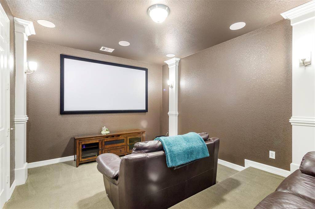 Media room features plush carpet, custom paint, high ceilings, speakers, and custom lighting.