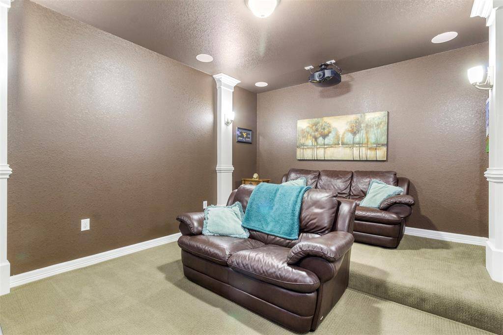 Media room features plush carpet, custom paint, high ceilings, speakers, and custom lighting.