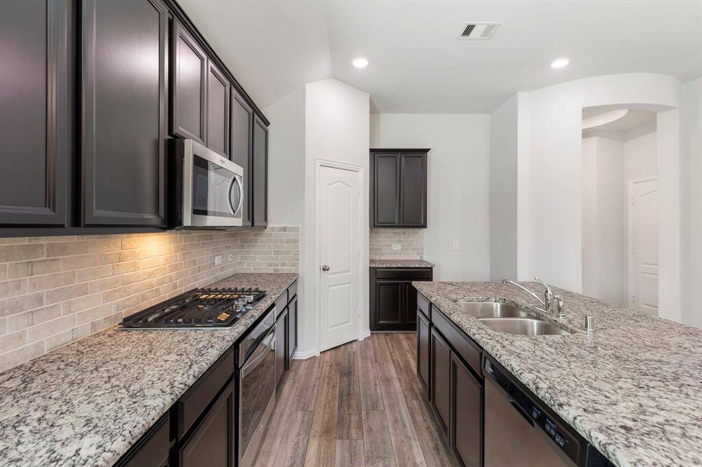 The island kitchen features leather texture finish granite countertops, stainless steel appliances, a gas cooktop, and plenty of storage space with the earth toned cabinets.