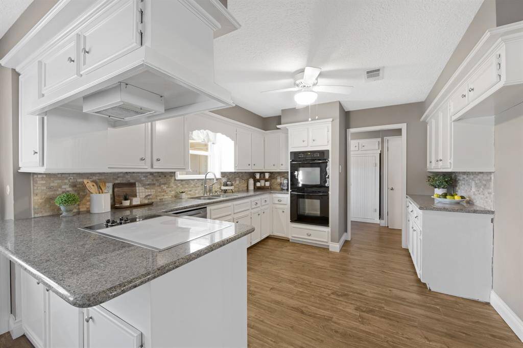 The kitchen is a chef's dream, featuring sleek granite countertops and crisp white cabinets with stylish hardware for a modern touch. Double ovens and a stunning Travertine backsplash complete the space, making it both functional and visually striking for cooking and entertaining.