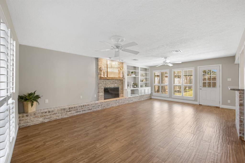 The beautifully spacious family room is designed for both comfort and style, featuring plantation shutters that allow for controlled natural light. A stunning brick fireplace serves as a focal point, complemented by built-in shelves and cabinets for extra storage, while two ceiling fans ensure the room stays cool and inviting year-round.