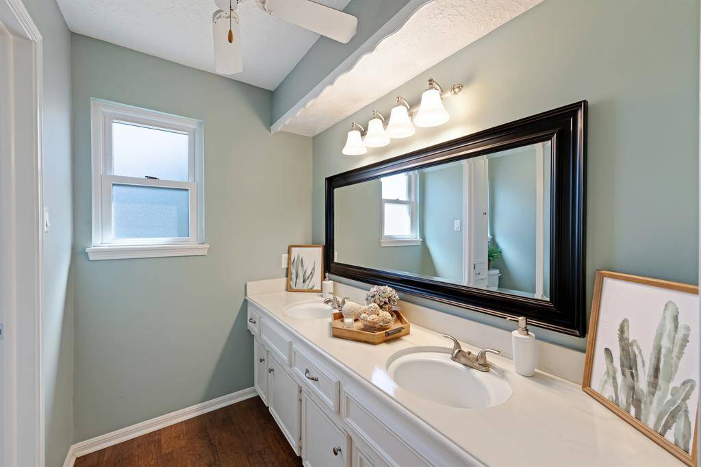 The secondary bathroom is thoughtfully designed with dual sinks and a framed mirror, offering both style and functionality. A ceiling fan adds comfort, making it a pleasant space for daily use.