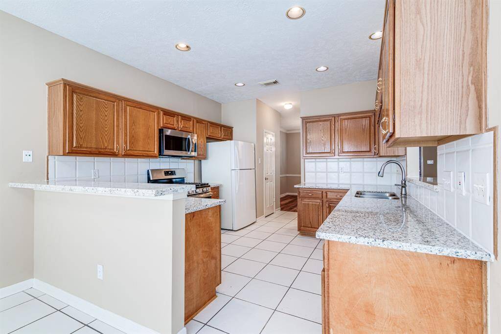 This kitchen features spacious wood cabinetry, granite countertops, and modern stainless steel appliances, including a microwave and stove. The tiled floor and recessed lighting provide a bright and functional space.