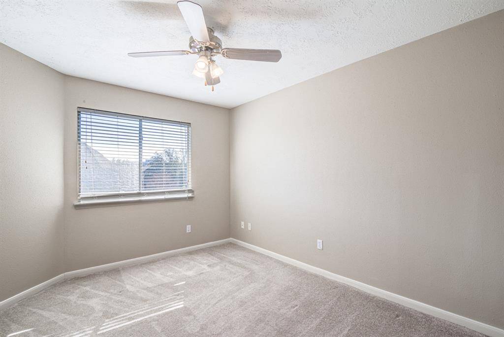 Bright, neutral-toned bedroom with a ceiling fan and large windows, offering plenty of natural light. Ideal for a bedroom or office space.