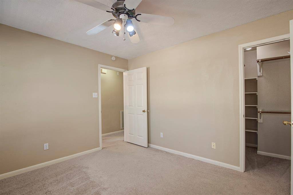 The first bedroom to your right as you enter upstairs is carpeted with beige walls and a ceiling fan. It has a walk-in closet with shelving. The space is well-lit and is perfect for a guest bedroom or office!