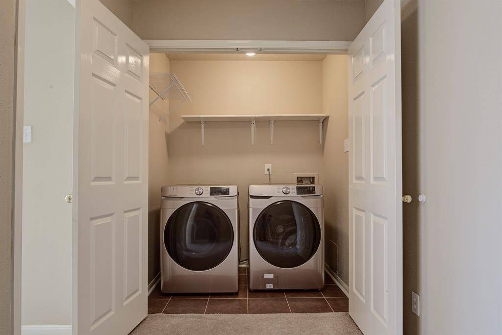 This photo shows a compact laundry closet with modern front-loading washer and dryer units. The space includes overhead shelving for storage and is enclosed by double doors, offering a neat and efficient setup for laundry needs.