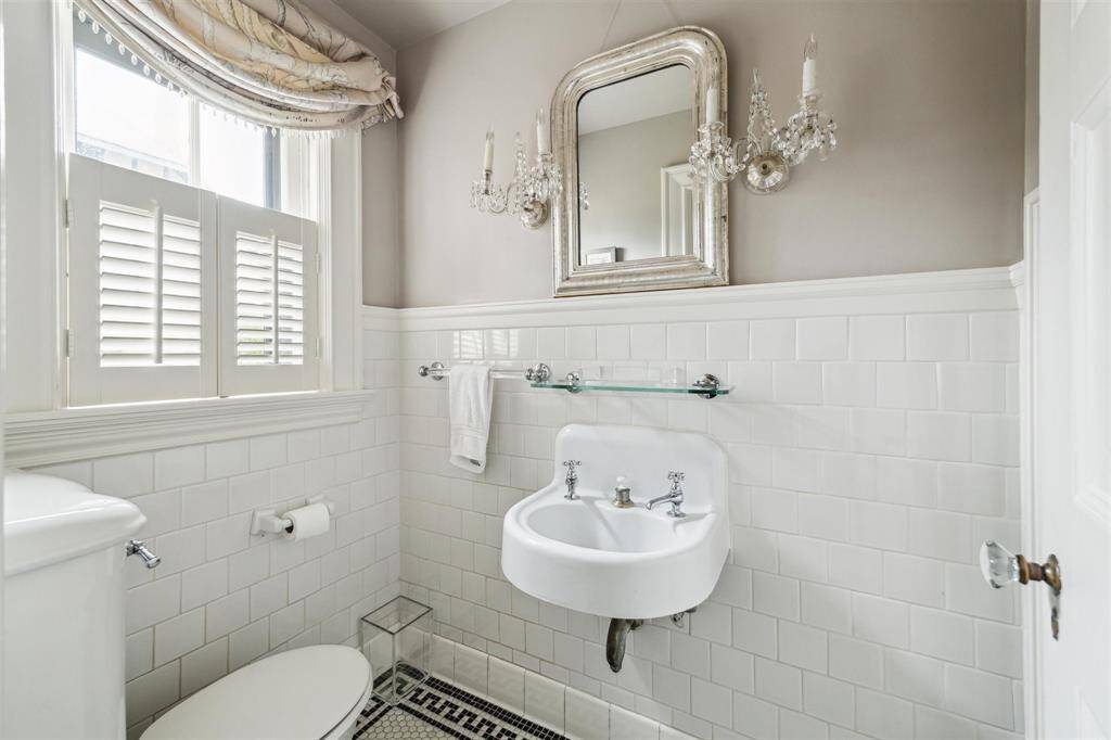 This charming water closet features classic subway tile wainscoting, a vintage wall-mounted sink, and crystal sconces that add a touch of elegance.
