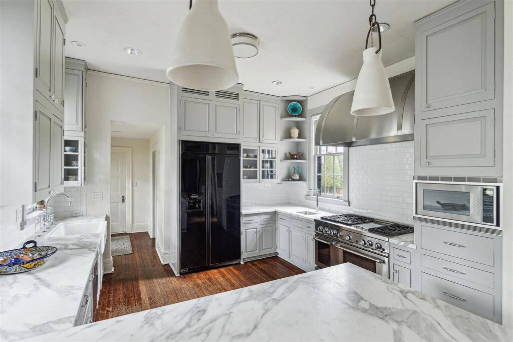 This angle of the kitchen highlights a bright, functional space, featuring marble countertops, custom cabinetry, and high-end appliances, complemented by sleek subway tile and ample natural light.