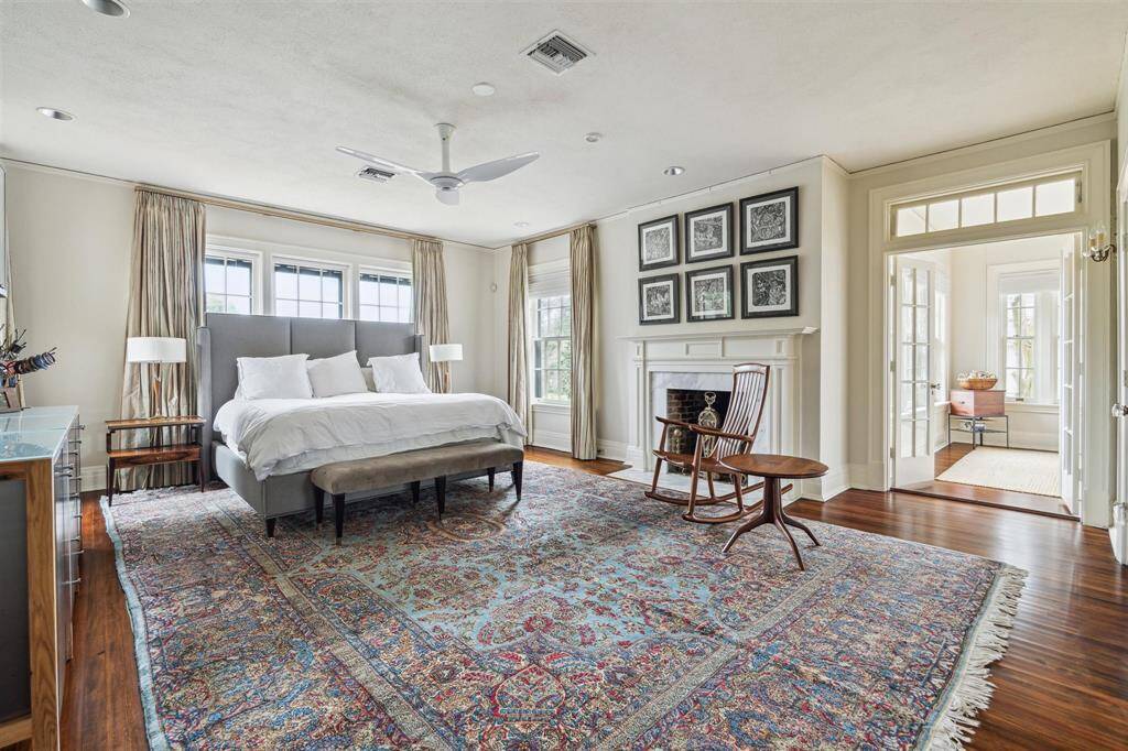 This expansive primary bedroom is a serene retreat, featuring abundant natural light, rich hardwood floors, and a cozy fireplace as a focal point. French doors lead to a sunlit sitting area, while elegant details and a spacious layout create a perfect blend of comfort and sophistication.