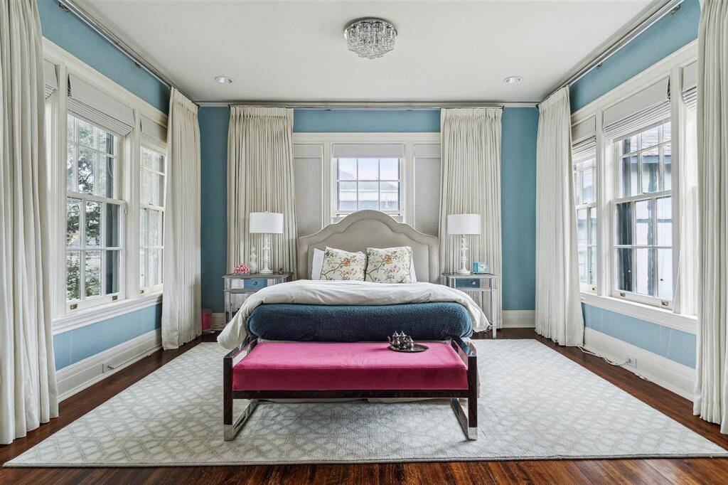 Awash in natural light, this delightful second bedroom features soft blue walls complemented by crisp white window treatments and gleaming hardwood floors. Large windows on three sides create a bright and airy ambiance, while elegant details, including a statement chandelier, add a touch of sophistication.