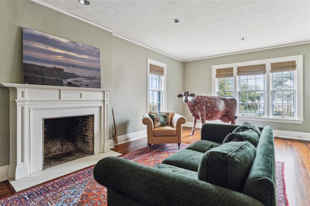 Currently serving as a cozy upstairs living area, this versatile third bedroom features a classic fireplace as its centerpiece, complemented by large windows that fill the space with natural light. The room’s warm tones and polished hardwood floors make it an inviting and adaptable retreat.