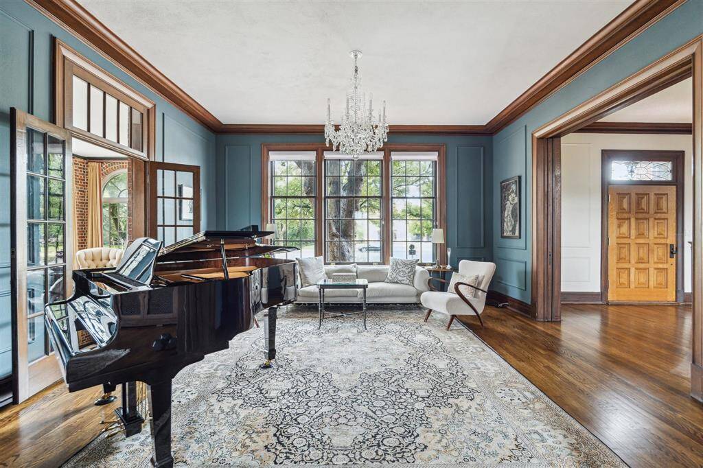 This stunning formal living room exudes elegance and charm, featuring rich teal walls accented with refined wood trim. The space is illuminated by natural light from oversized windows and has pocket doors at the entry points for ease of openness or privacy.