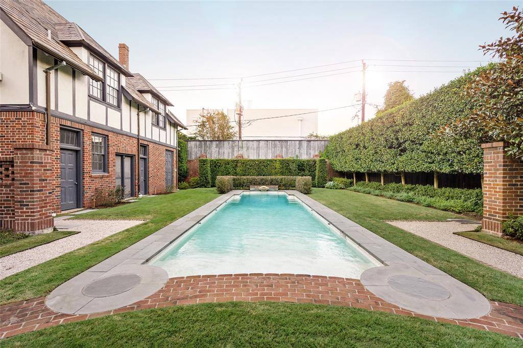 This pristine pool is the centerpiece of a beautifully landscaped backyard oasis. Surrounded by manicured hedges and lush greenery, the pool offers a serene escape with its classic rectangular design and inviting water. Brick accents, a water feature, and bench seating area add charm and functionality, making it perfect for both relaxation and entertaining.