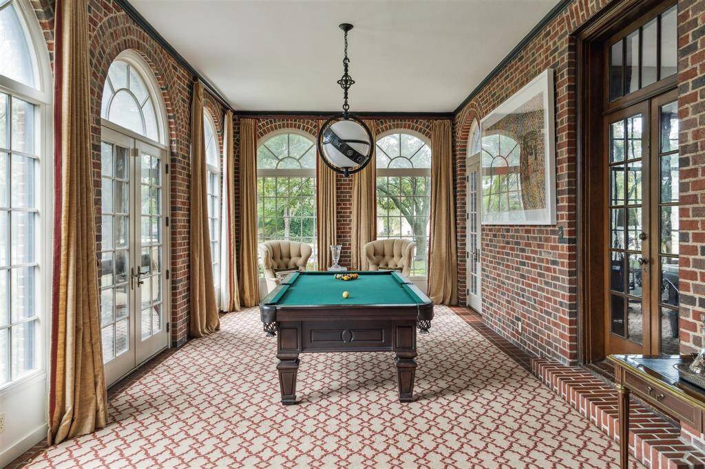 This refined sunroom boasts a timeless design with brick walls and arched windows that let in abundant natural light. A chic Visual Comfort Zodiac pendant light enhances the room's character while French doors open to the outdoors, blending indoor and outdoor living seamlessly. A perfect space for entertaining or unwinding, this sunroom exudes charm and versatility while maintaining its classic elegance.