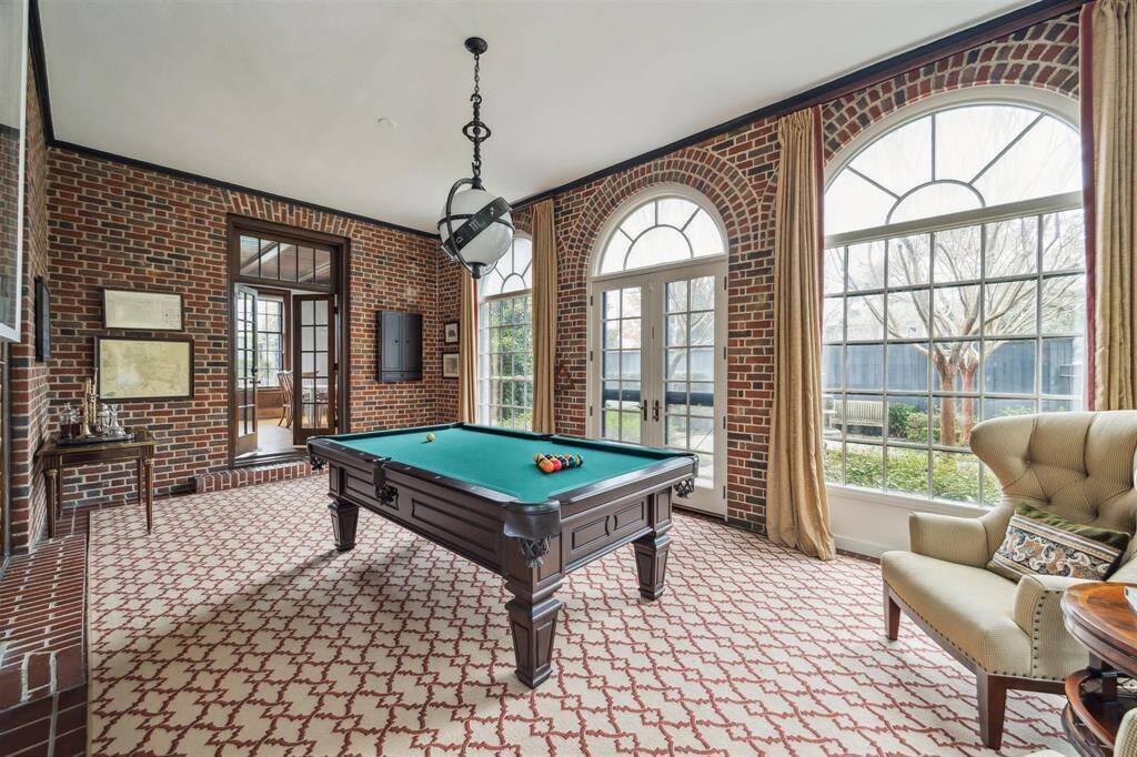 Surrounded by striking arched windows and rich brick walls, this versatile space is perfectly suited for a pool table, offering a seamless blend of function and charm. French doors provide easy access to the outdoors, while additional interior doors lead to adjacent rooms, making it an ideal hub for entertaining or casual gatherings.