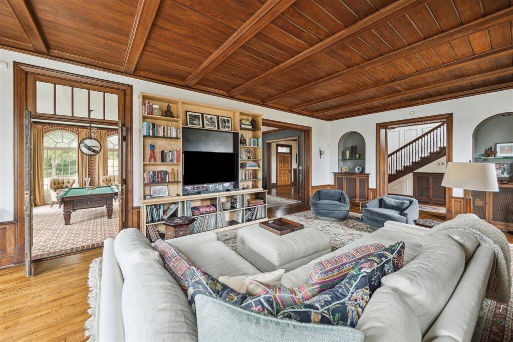 Back inside, a spacious family room features a stunning coffered wood ceiling and rich architectural details, including arched alcoves and elegant wood trim. Double doors lead seamlessly to the adjacent sunroom, with pocket doors leading to the living room, enhancing the room’s versatility and flow.