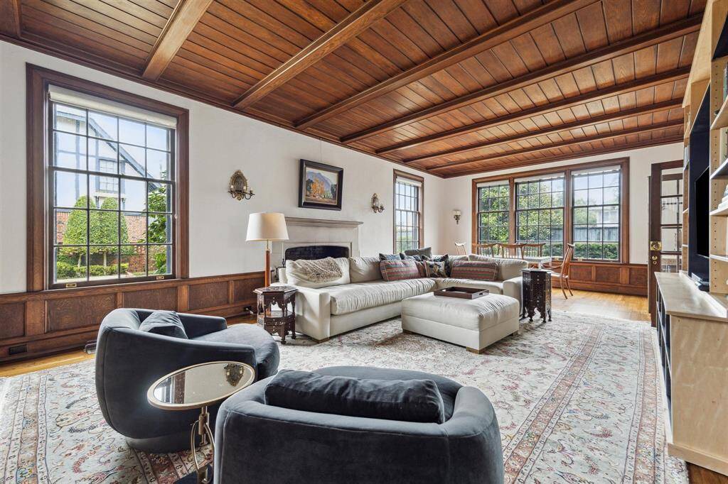 Expansive windows, a coffered wood ceiling, and rich paneling create a warm and inviting atmosphere in this beautifully detailed living space, complemented by a stunning limestone surround that frames a cozy wood-burning fireplace. This elegant focal point adds both warmth and a touch of sophistication, making the space perfect for gatherings or quiet evenings at home.