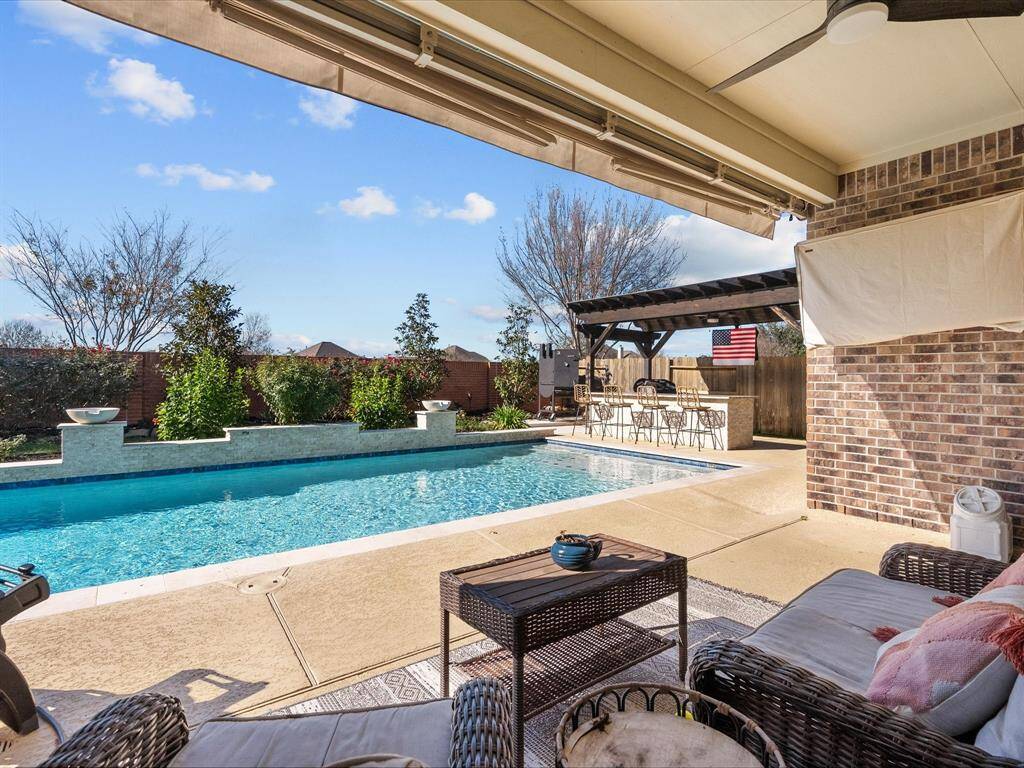 The covered patio offers a shaded retreat overlooking the swimming pool. Awning provides comfort, and the outdoor kitchen is perfect for poolside gatherings.