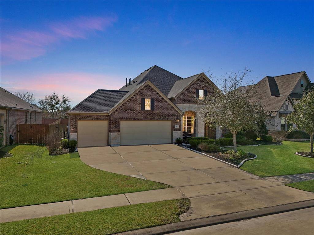This wide shot highlights the home's symmetrical design, featuring a triple garage and a neatly landscaped front yard.  The brick and stone accents provide a classic and timeless aesthetic.