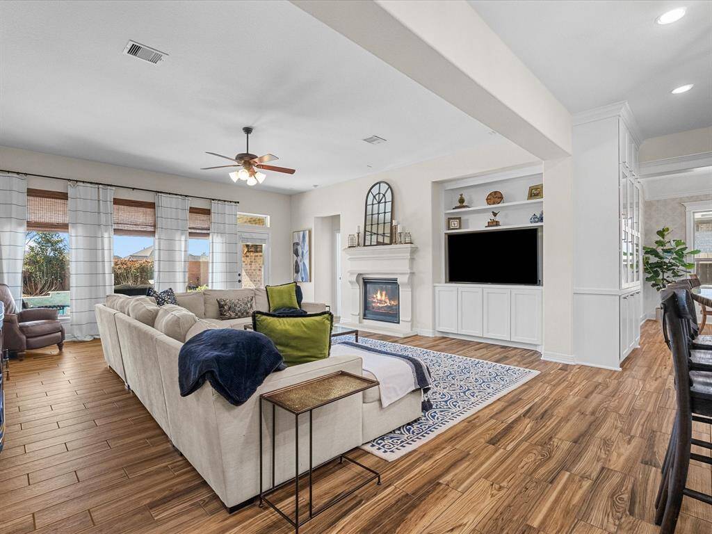 The living room features a built-ins with updated shaker style cabinets and a cast stone fireplace, creating a focal point. The open layout seamlessly connects to the kitchen and breakfast room, offering a spacious and inviting area.