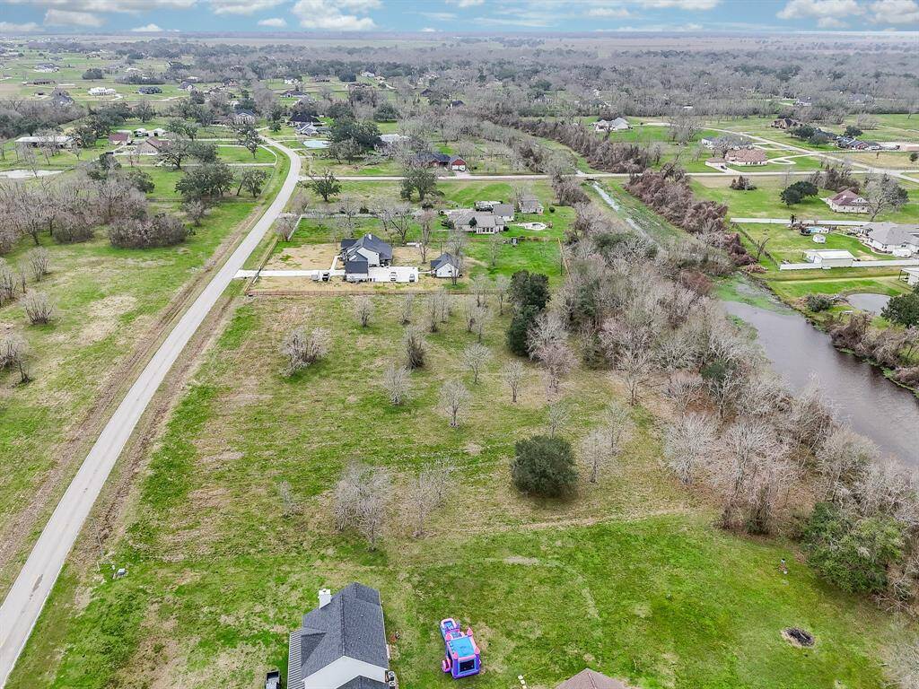 This aerial photo showcases a spacious area with scattered homes. A winding road runs through the landscape, surrounded by large grassy fields and patches of trees. Water body can be seen on the right, adding a natural touch to the serene setting. Ideal for those seeking a peaceful, countryside environment.