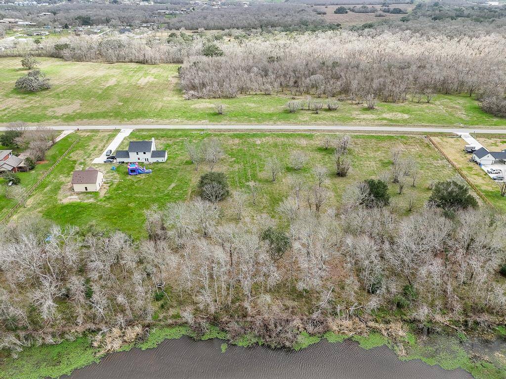 This aerial photo showcases a spacious residential lot nestled by water, surrounded by lush greenery and mature trees.