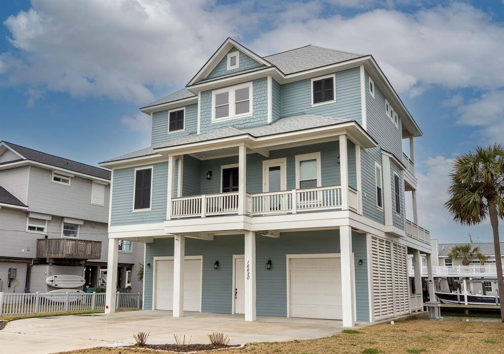 Experience coastal charm in this custom-built home with a light blue exterior and white trim. Featuring a spacious two-car garage, elevated design, and a large balcony, it's surrounded by lush greenery and palm trees, offering a picturesque and inviting setting.