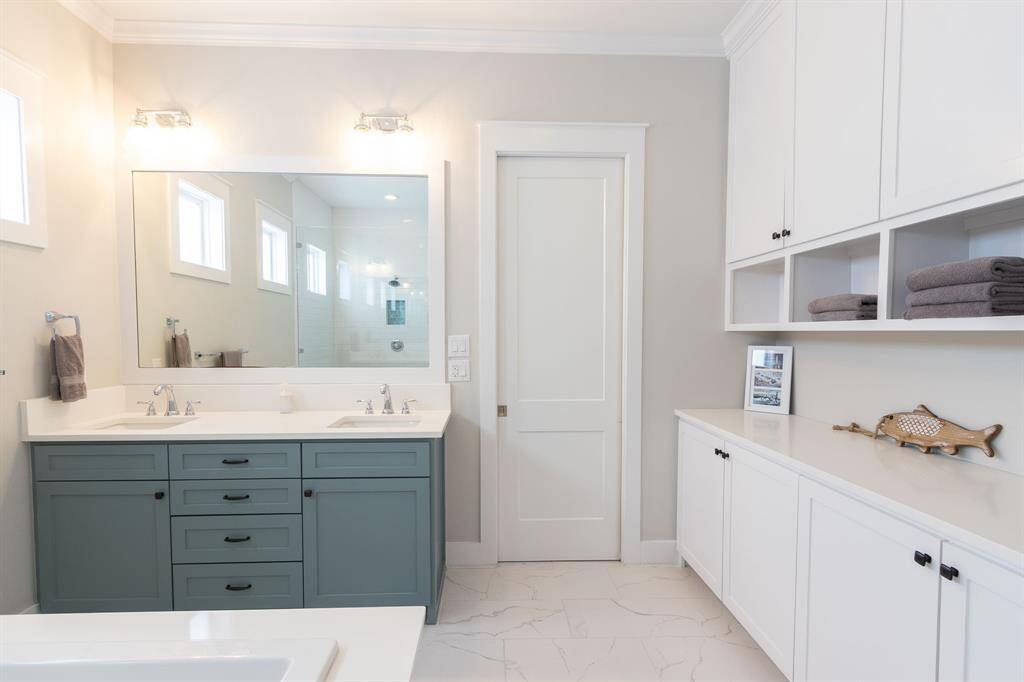 This bathroom features a sleek, modern design with white cabinetry and open shelving. It includes a spacious bathtub and a glass-enclosed shower. Natural light filters through small windows, creating a bright and inviting space.