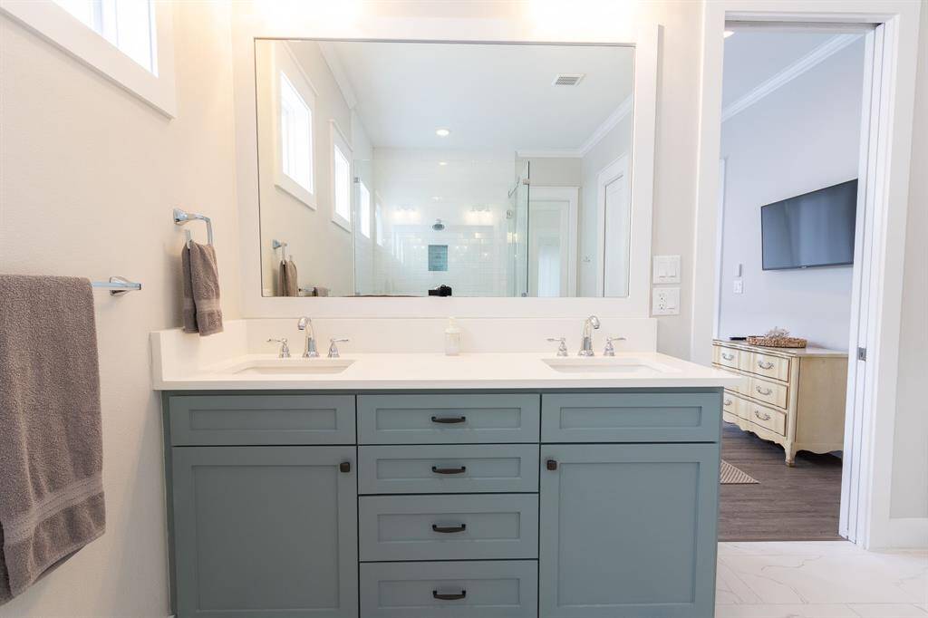 .This bathroom features a sleek, modern design with white cabinetry and open shelving. It includes a spacious bathtub and a glass-enclosed shower. Natural light filters through small windows, creating a bright and inviting space.