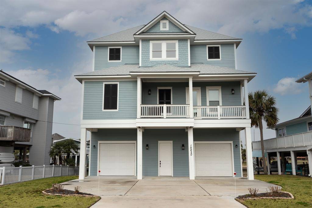Discover this custom built charming two-story coastal home with a striking blue exterior and white trim. Featuring a double garage and inviting front porch, it's nestled among lush greenery and palm trees, all under a bright blue sky.
