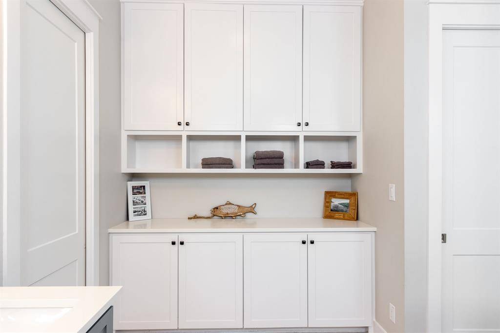 This photo shows a clean, modern storage area with white built-in cabinets and shelves. The space is neatly organized, featuring decorative items and folded towels, set against a neutral wall color. Ideal for extra storage or display.