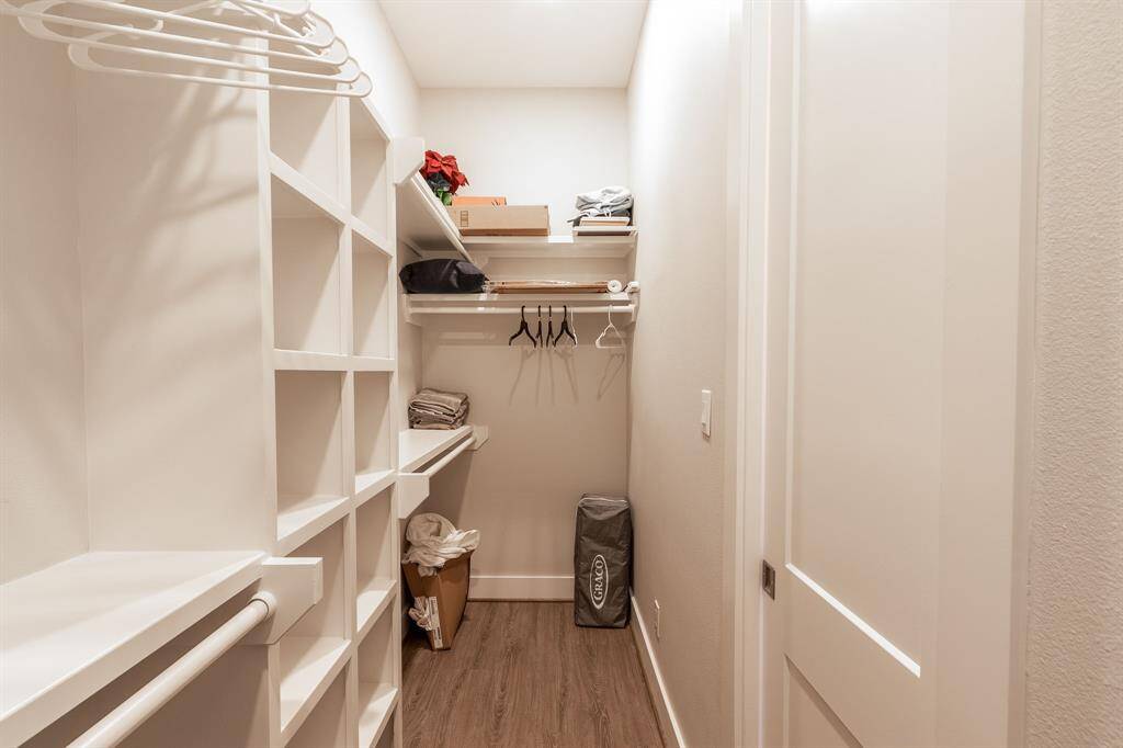 Expansive primary closet for all your storage needs!  This photo shows a spacious walk-in closet with built-in shelving and hanging rods, perfect for organized storage. The space is well-lit and features a wood-look floor.