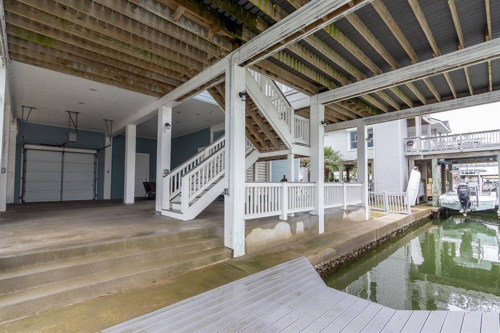 This photo shows a waterfront home with a covered boat slip and dock area. It features an open understructure with stairs leading to the main living area, offering ample space for parking and outdoor activities. The setting is ideal for boating enthusiasts looking for direct water access.