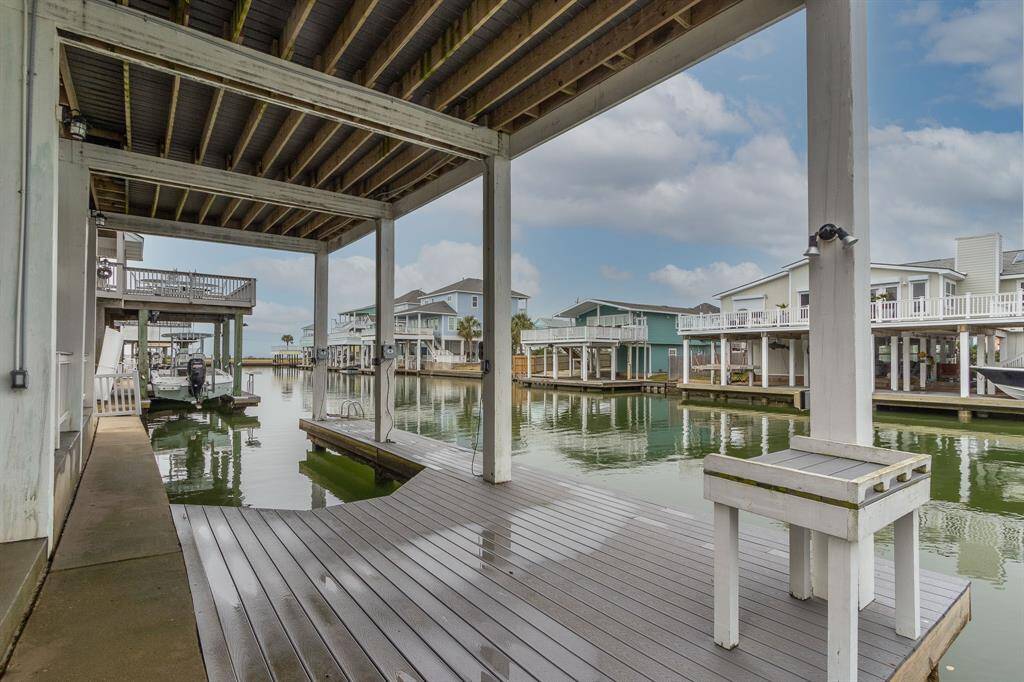 This photo shows a waterfront home with a covered boat slip and dock area. It features an open understructure with stairs leading to the main living area, offering ample space for parking and outdoor activities. The setting is ideal for boating enthusiasts looking for direct water access.