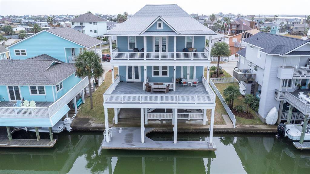This photo showcases a charming custom waterfront property with a spacious wraparound porch, offering picturesque views of the canal. The house is elevated, featuring multiple levels and surrounded by lush greenery, providing a serene and inviting atmosphere for potential home buyers.