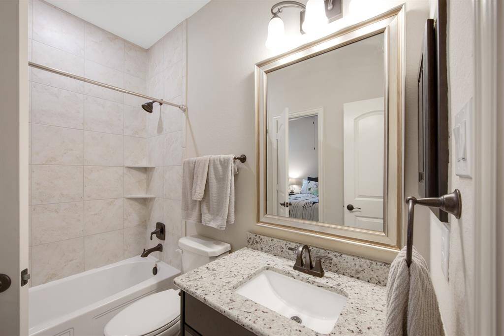 First of the two identical upstairs full bathrooms with tile flooring, tile tub/shower combo, elongated toilet, granite counter sink, designer framed mirror and medicine cabinet