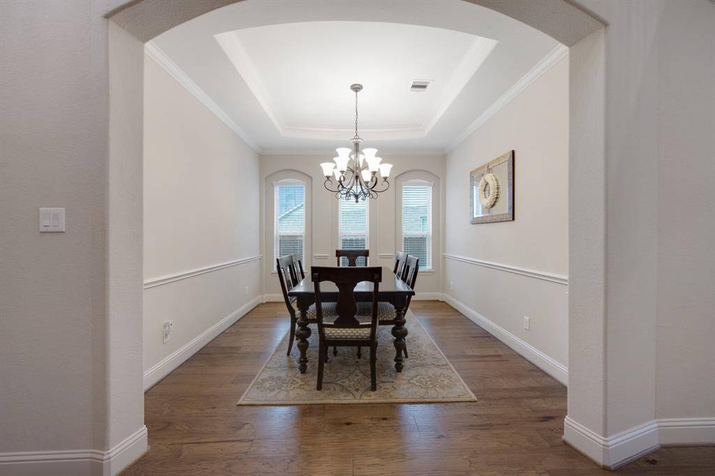 Another picture of the dining room with arched entry, three arched windows, stunning wood flooring, crown molding and wide base boards.