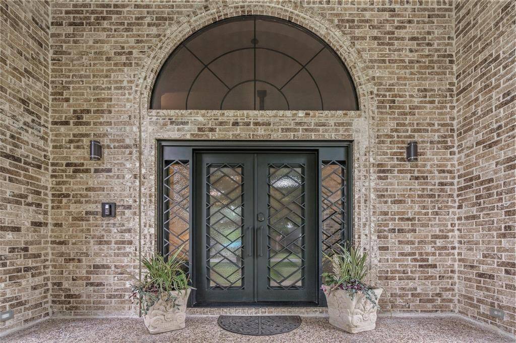 Welcoming brick entryway with elegant double doors featuring decorative glass and an arched transom. Two stylish planters add a touch of greenery.