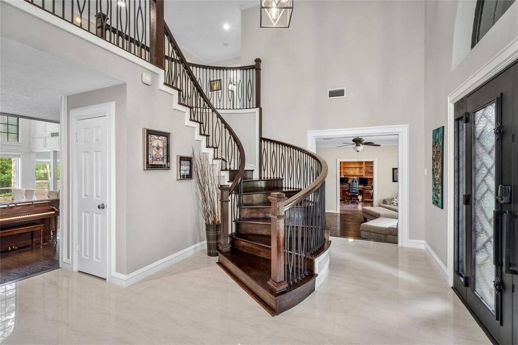 Welcome home to a grand foyer featuring a stunning dark wood spiral staircase, high ceilings, and polished tile floors. This elegant entryway leads to a cozy living area and a charming piano room, adding a touch of luxury.