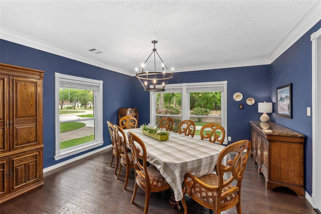 Experience the charm of this dining room with rich blue walls, elegant crown molding, and expansive windows showcasing scenic views. The wooden dining set, classic cabinetry, and modern chandelier create a warm, inviting ambiance.