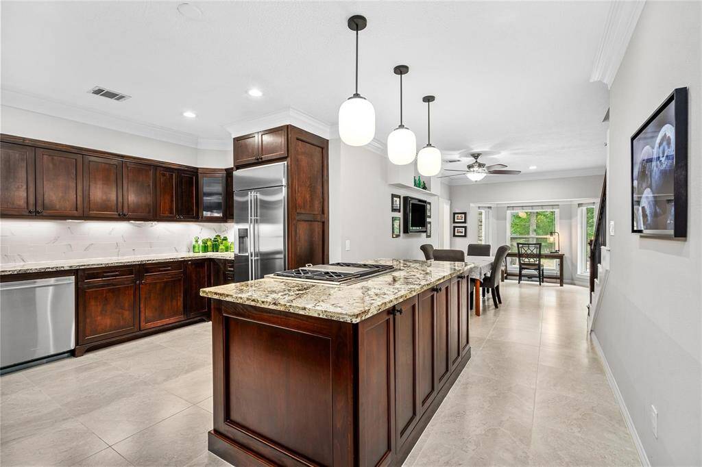 Experience this modern kitchen and dining area with rich dark wood cabinetry, sleek stainless steel appliances, and a central island illuminated by stylish pendant lights. The open layout flows seamlessly into a bright dining space, enhanced by large windows for an inviting atmosphere.