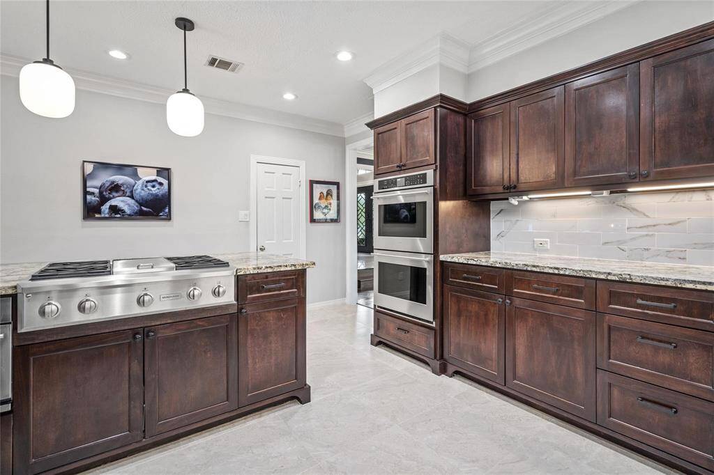 Elegant kitchen with dark wood cabinetry, stainless steel appliances, and granite countertops. Features modern lighting, a built-in oven, and a spacious cooktop for a stylish, functional space.