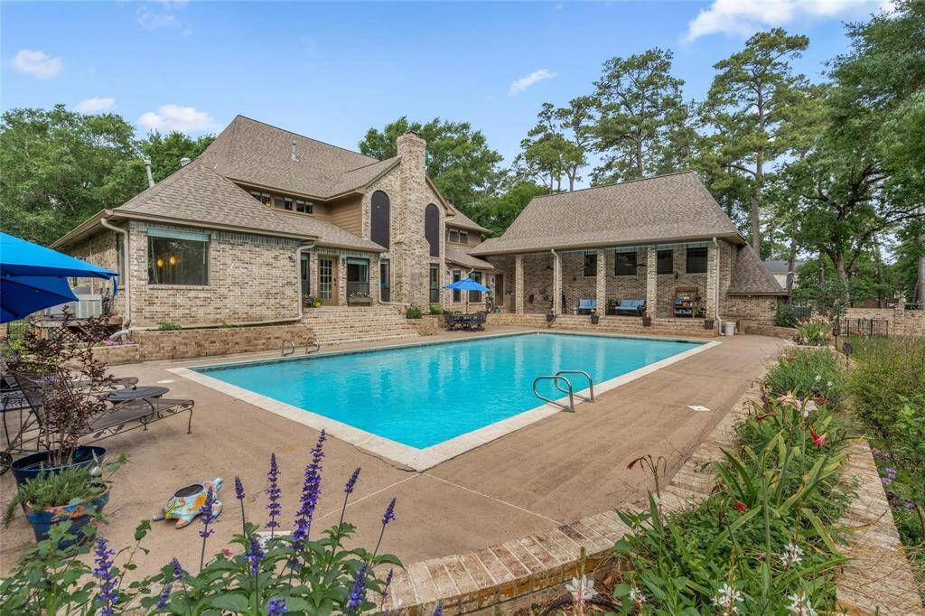 Discover a stunning backyard oasis featuring a large swimming pool and beautifully landscaped patio. The charming brick home boasts multiple gables and expansive windows, offering elegance and warmth. Perfect for entertaining, with ample seating areas set against a backdrop of mature trees.