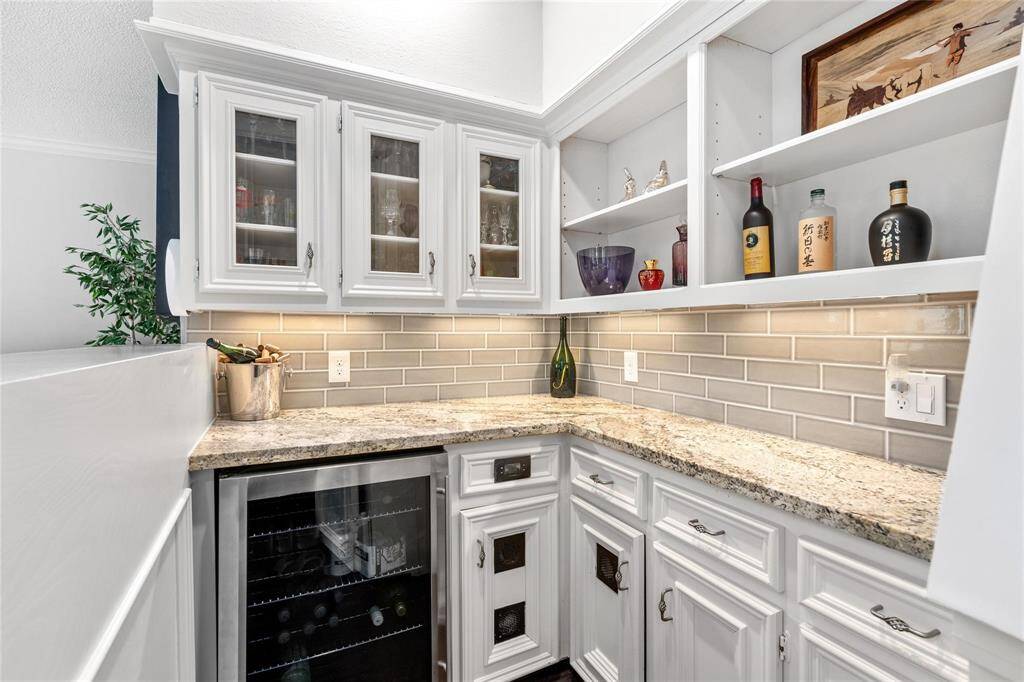 Experience elegance with this stylish wet bar, featuring white cabinetry, granite countertops, a built-in wine cooler, and a sleek subway tile backsplash—perfect for entertaining.