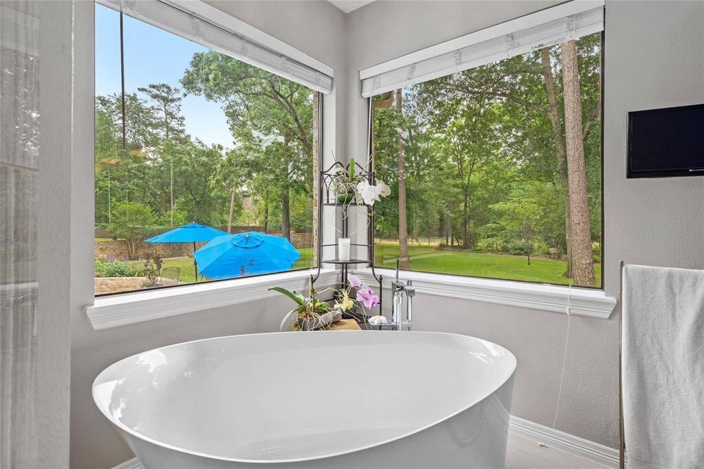 This bathroom offers a serene, spa-like experience with a modern freestanding tub surrounded by large windows showcasing a lush, green backyard. The space is bright and airy, providing a peaceful retreat with views of nature.