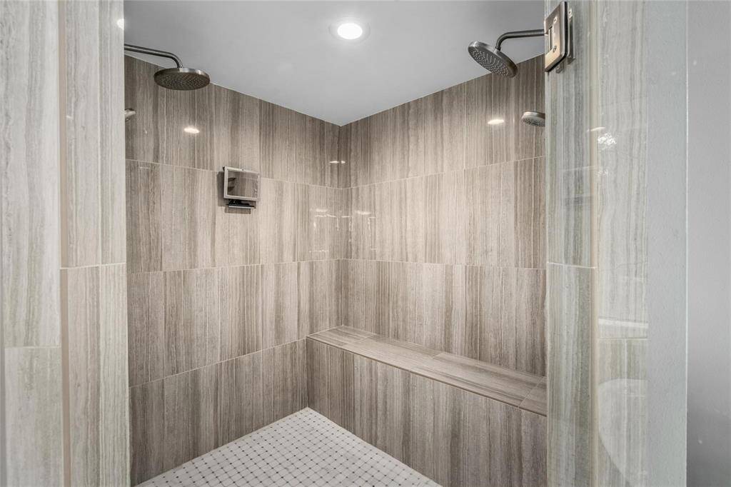 Spacious double shower with elegant gray tile, dual rain showerheads, and a built-in bench for comfort and convenience.