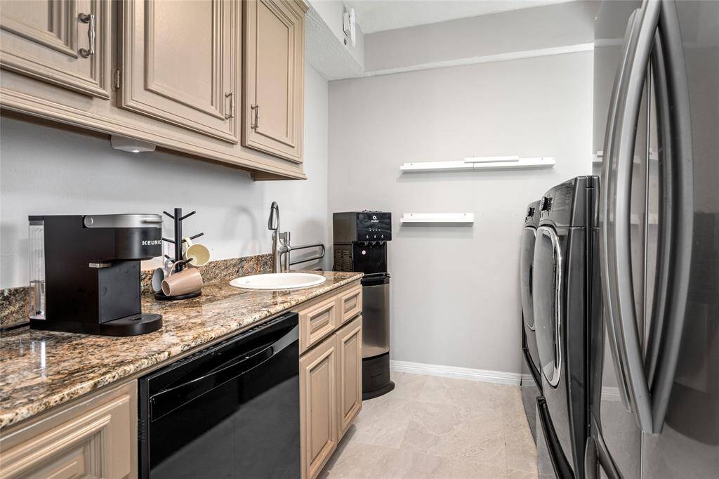 Discover a stylish and functional laundry room featuring sleek granite countertops, elegant wooden cabinets, and modern appliances, including a washer, dryer, and coffee maker.
